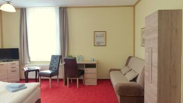 A hotel room with a bed, a desk, a chair, a sofa, a wardrobe, a television, and a window with curtains.