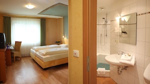 Een hotelkamer met een bed, een bureau met stoel, een televisie en een badkamer met wastafel, spiegel en douche.