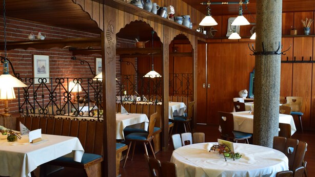 Een restaurant met houten wanden, bakstenen details en meerdere tafels met witte tafellinnen.