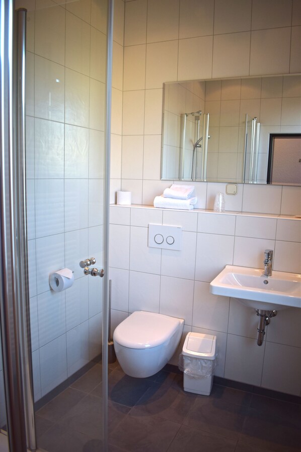 A modern bathroom with a toilet, sink, and glass shower enclosure. - Landgasthof Buch (Eichenzell)