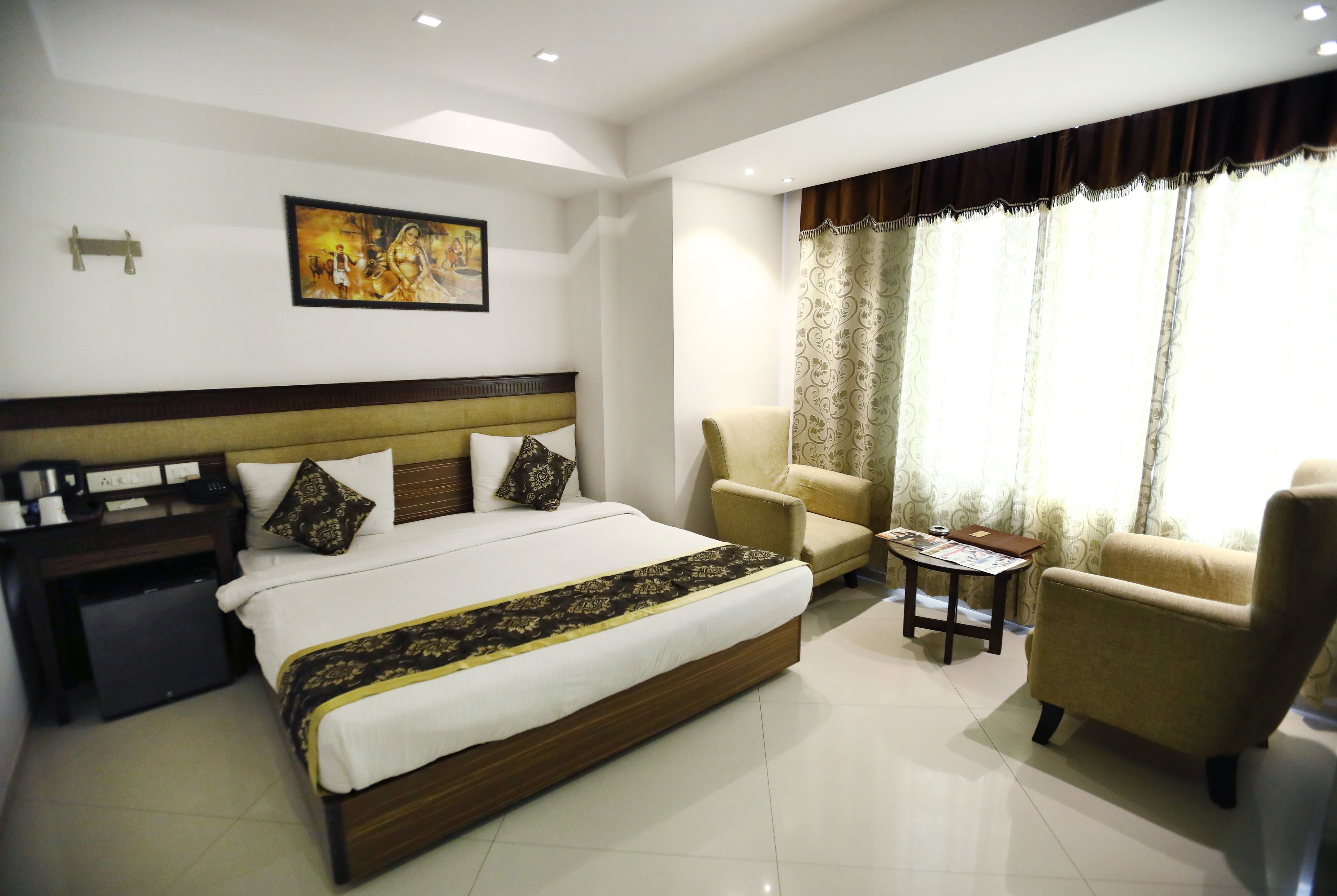 A hotel room with a large bed, two armchairs, a small table, and a painting on the wall.