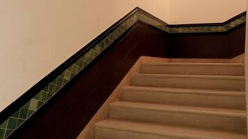 Una escalera con barandal de madera oscura y escalones color beige, que conduce a un rellano con una lámpara.