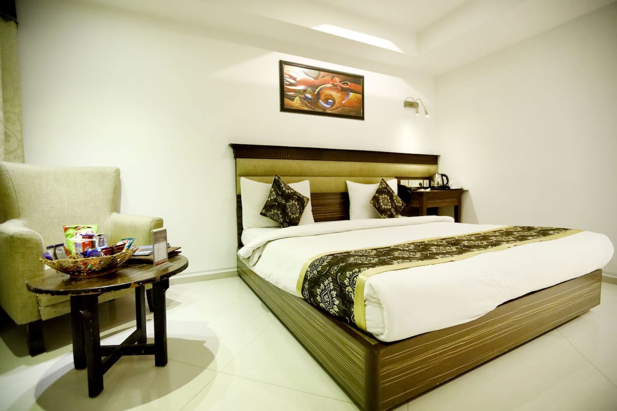 A hotel room with a large bed, a small table with a basket, a chair, and a painting on the wall.
