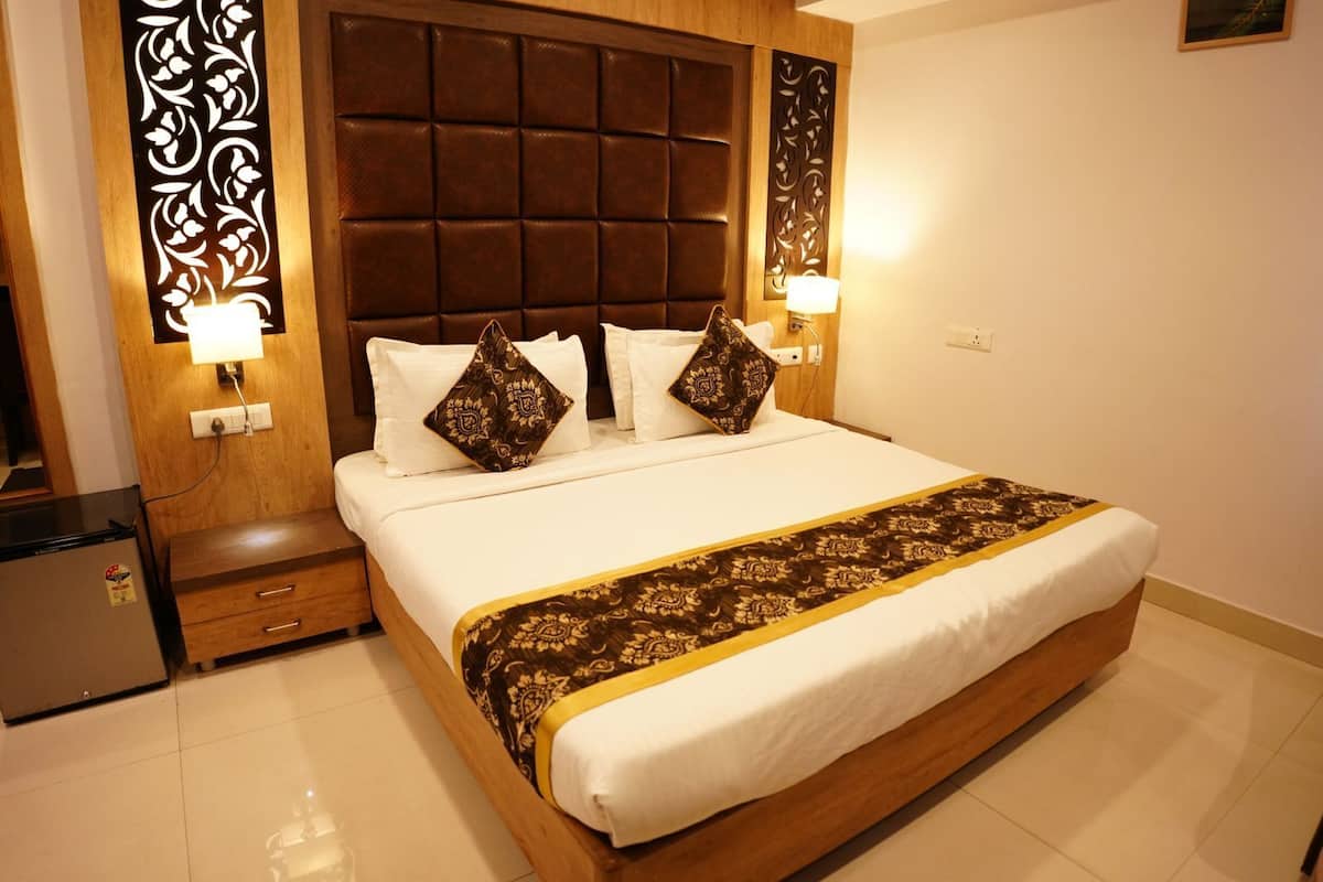 A hotel room with a large bed, wooden headboard, two bedside lamps, a nightstand, and a small refrigerator.
