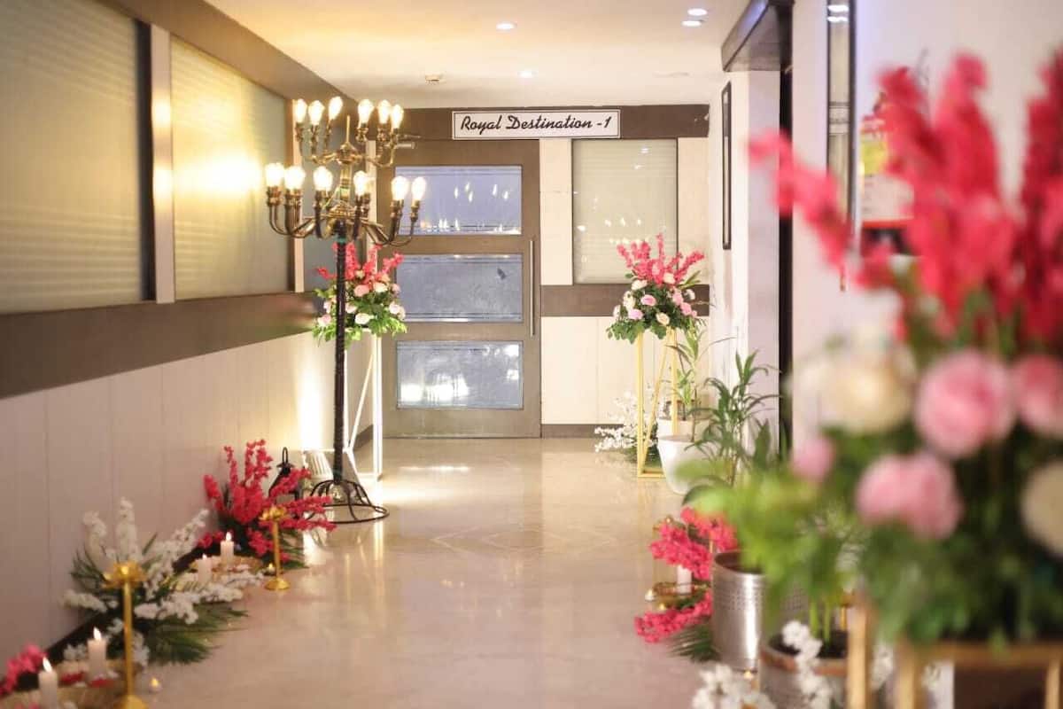 A hotel lobby with a chandelier, floral arrangements, and a sign reading 'Royal Destination - 1'.