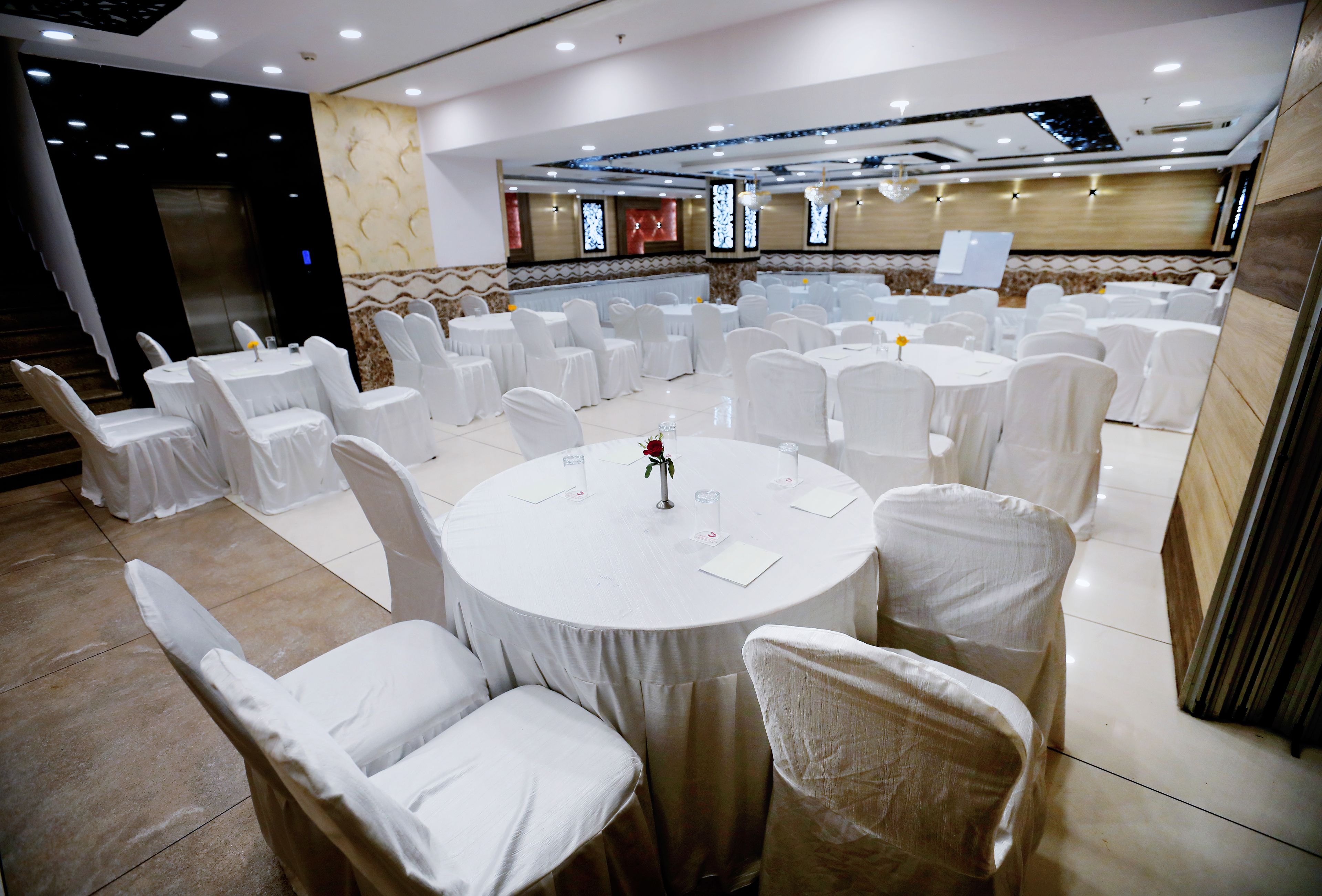 A banquet hall with round tables and white chairs, a staircase, and a decorative wall with a clock.