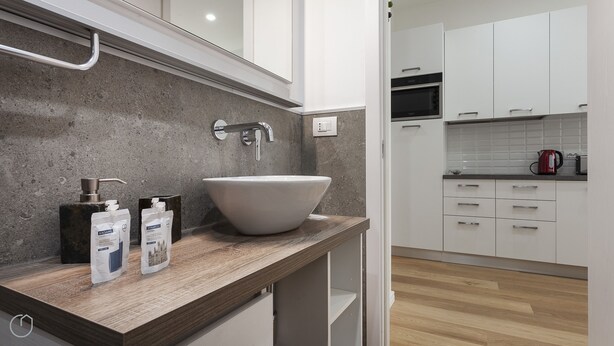 A modern bathroom with a large white sink, a handheld showerhead, and toiletries on the countertop. - Italianway   - Segrino 6 (Milan)