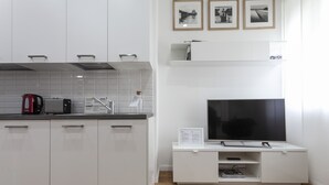 A modern kitchen with white cabinets, a black toaster, a red kettle, and a built-in TV on a white stand. - Italianway   - Segrino 6 (Milan)