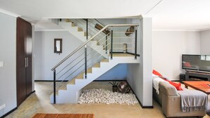 A modern living room with a staircase, a sofa, a coffee table, and a flat-screen TV. - Coral Sands Brickstone (Cape Town)