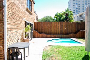 A backyard with a swimming pool, a wooden fence, and a brick building.