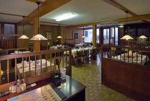 A restaurant with multiple dining areas, wooden railings, and hanging lamps. Tables are set with white tablecloths and chairs. - Hotel Restaurant Schütz (Trier)