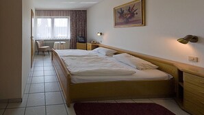 A hotel room with a large bed, bedside tables, a desk, a chair, and a window with curtains. - Hotel Restaurant Schütz (Trier)