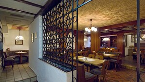 A restaurant with a high ceiling, patterned ceiling, and a decorative metal partition. There are tables and chairs arranged for dining. - Hotel Restaurant Schütz (Trier)