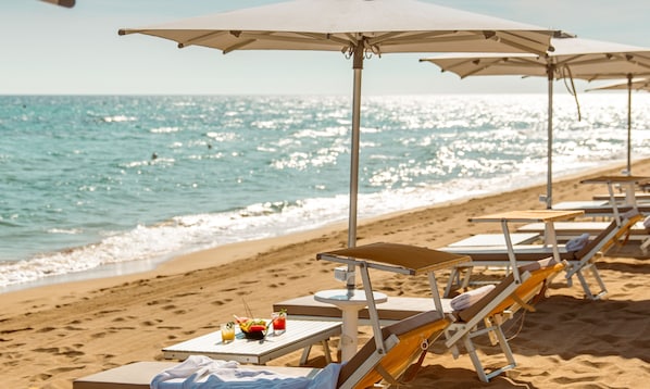 A beachside setting with sun loungers, umbrellas, and a table with a drink and fruit.