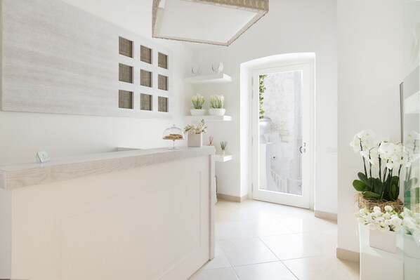 A modern reception area with a white reception desk, a large abstract painting, and a glass door leading to a balcony with a view of the outdoors.