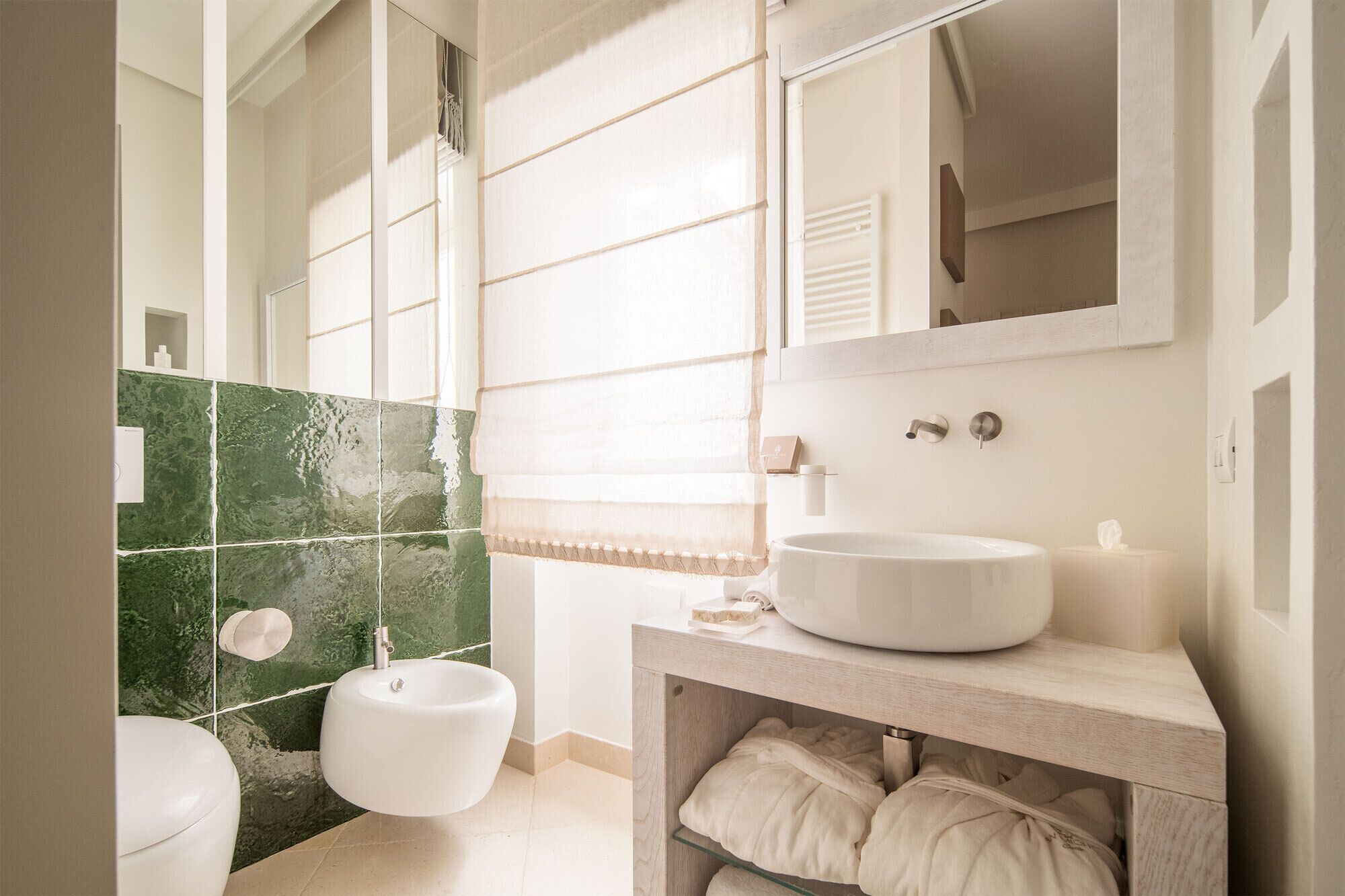A bathroom with a white sink, a bidet, and a toilet. There is a mirror above the sink and a towel rack on the wall.