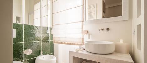 A bathroom with a white sink, a bidet, and a toilet. There is a mirror above the sink and a towel rack on the wall.