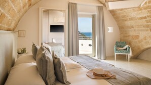 A bedroom with a stone ceiling, a bed with pillows, a hat, and a chair by the window. - San Michele Suite (Polignano a Mare)