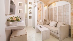 A modern, minimalist bathroom with a stone wall, a white vanity, a sofa, and a television. - San Michele Suite (Polignano a Mare)