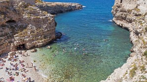 A coastal beach with clear water, rocky cliffs, and a stone building with a balcony overlooking the sea. - San Michele Suite (Polignano a Mare)
