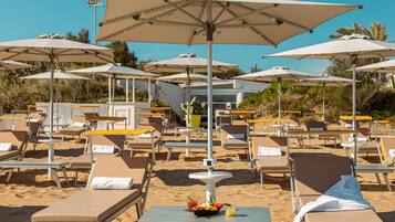 Een loungeruimte aan het strand met ligbedden, parasols en een tafel met een schaal fruit en een drankje.
