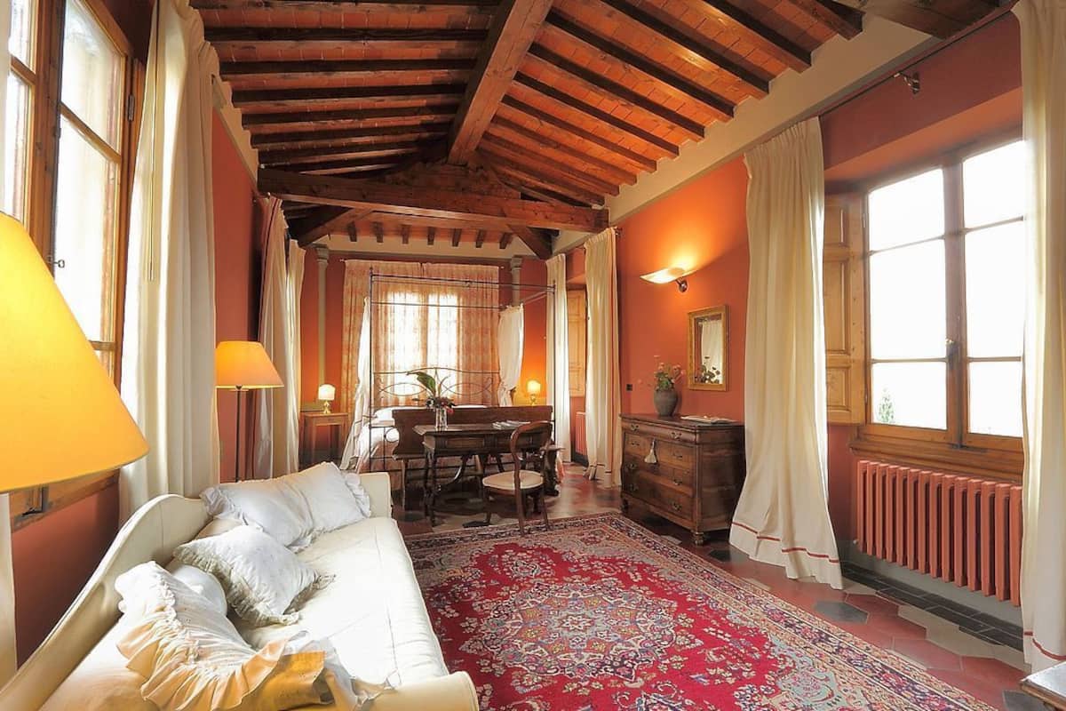 Ein Zimmer mit einem Bett, Holzboden, einem Esstisch mit Stühlen, einem Schminktisch und einem großen Fenster mit Vorhängen.