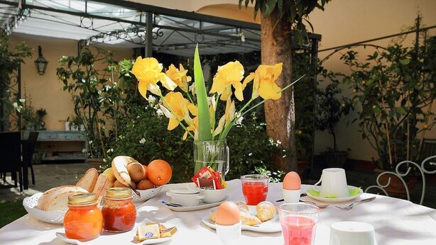 A breakfast table set outdoors with bread, eggs, fruit, and a vase of yellow flowers. - Villa Il Colle (Bagno a Ripoli)