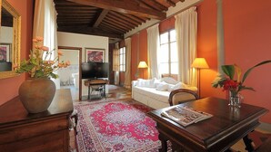 A cozy living room with a wooden ceiling, a large TV, a sofa, a coffee table, and a red patterned rug. - Villa Il Colle (Bagno a Ripoli)