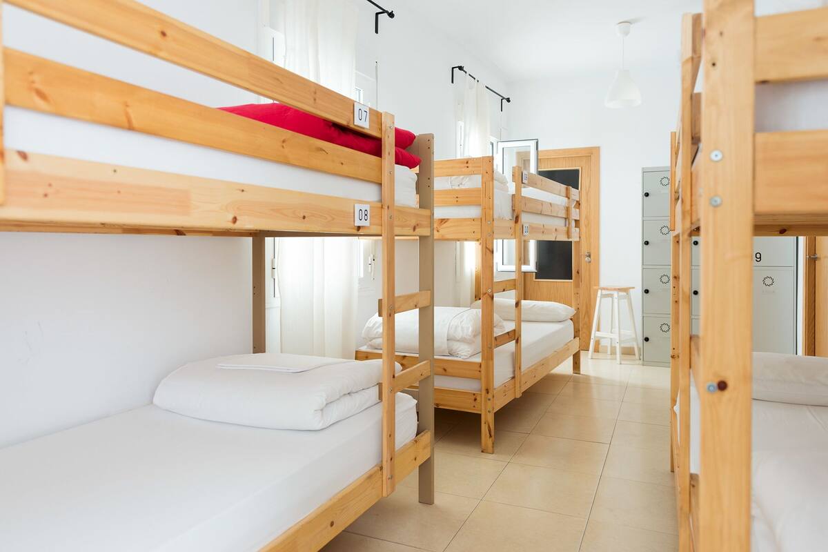 A dormitory room with bunk beds, a white door, and a small stool.