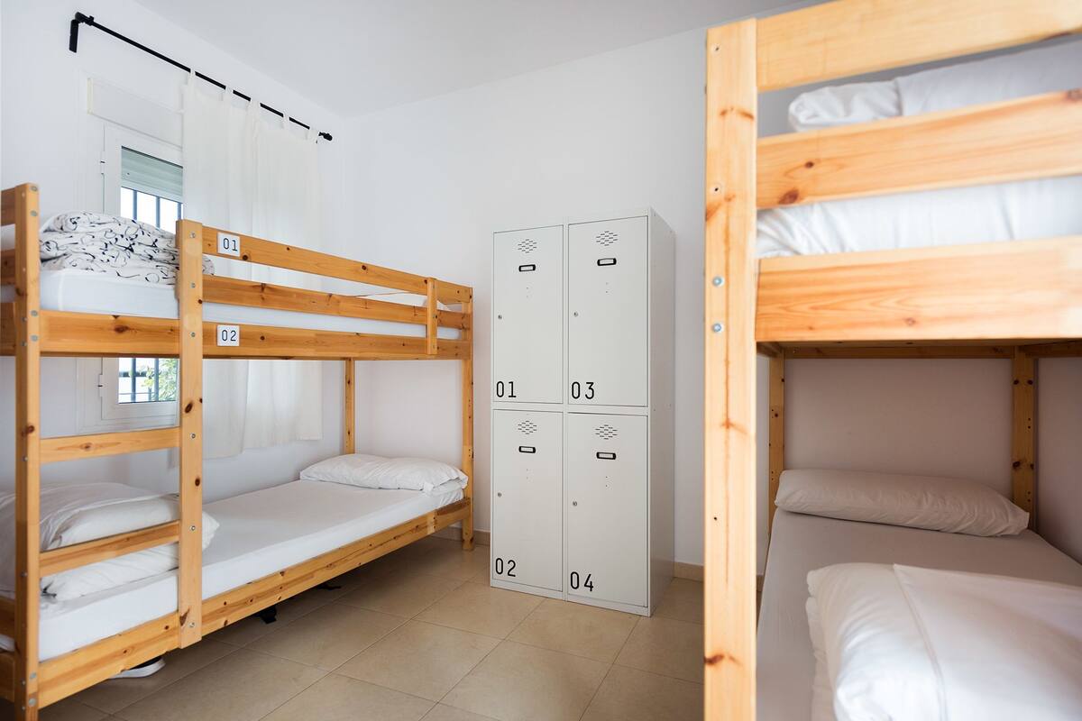 A dormitory room with bunk beds, a wardrobe, and a window with curtains.