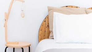 A bed with a wooden headboard, a round wooden stool, and a wooden floor lamp with a light bulb. - La Casa Morada - Hostel (Cádiz)