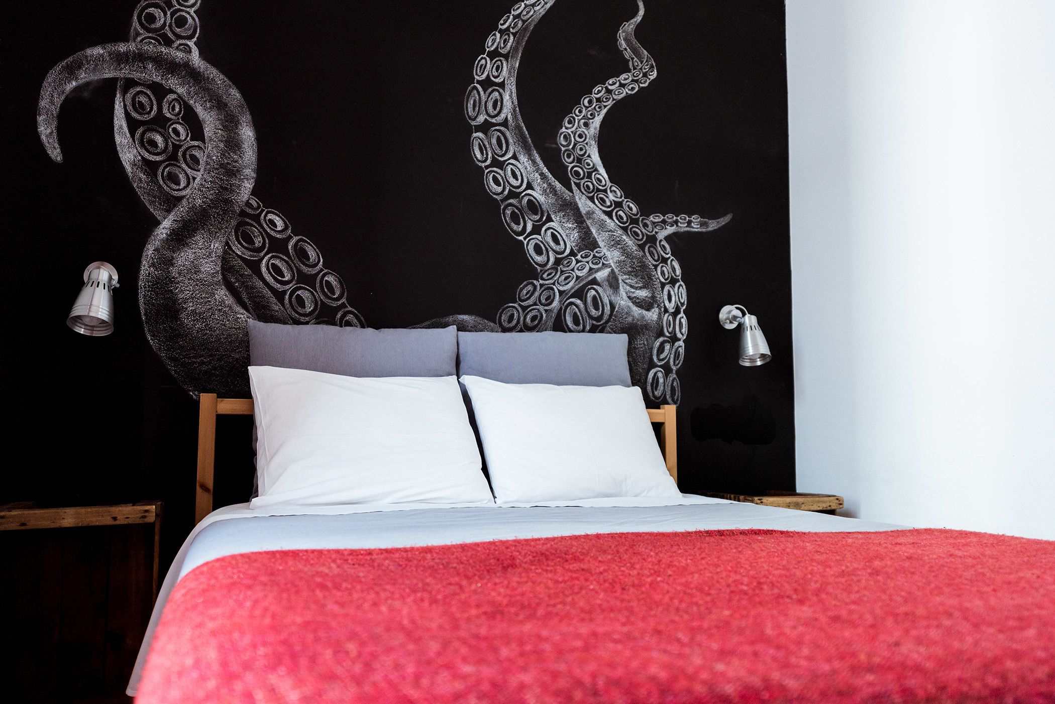 Una cama con una colcha roja, almohadas blancas y un cabecero con un diseño de pulpo en blanco y negro.