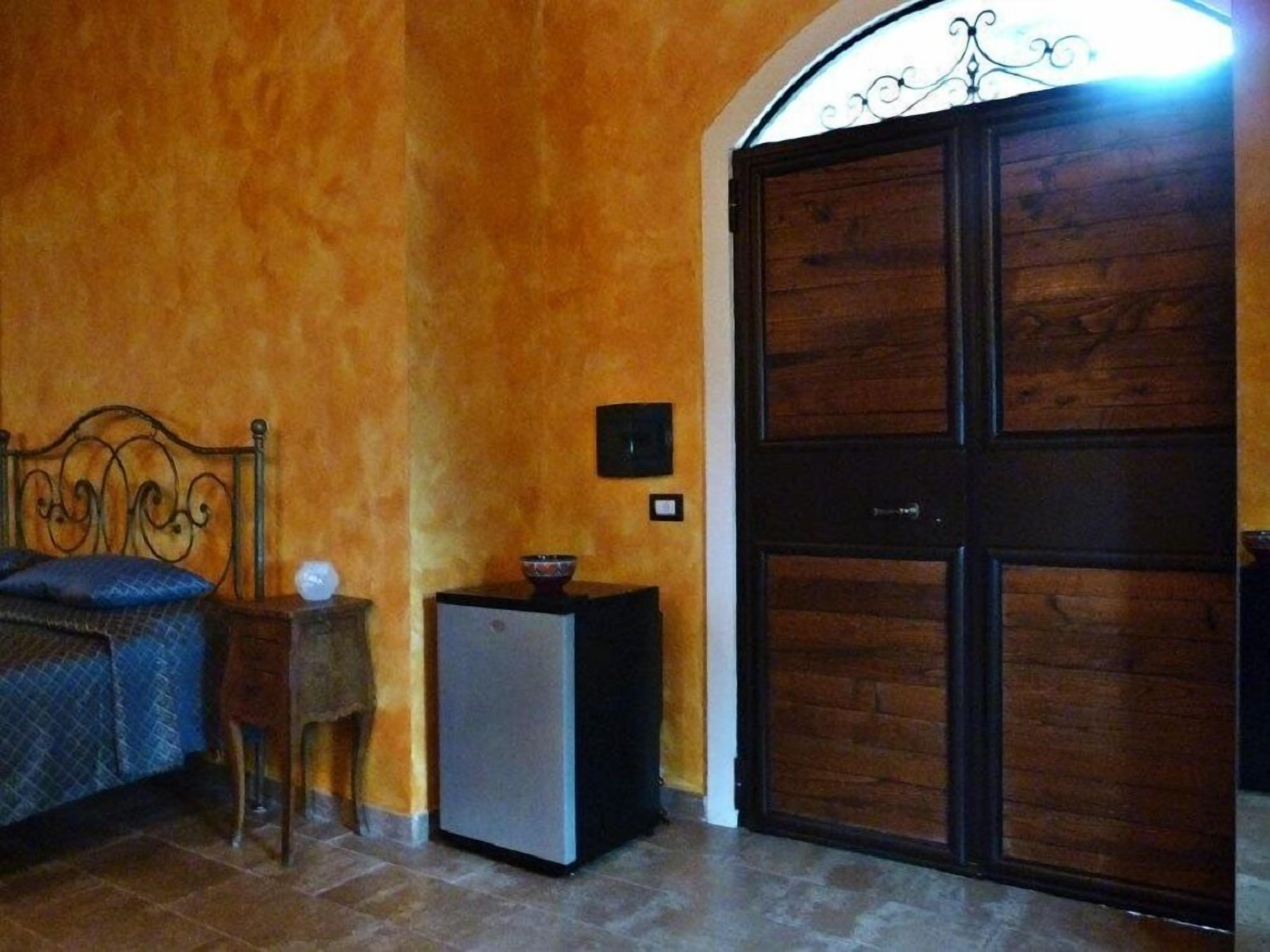 Ein Zimmer mit einem Bett, einem kleinen Tisch mit einer Schüssel, einem Kühlschrank und einer großen Holztür.