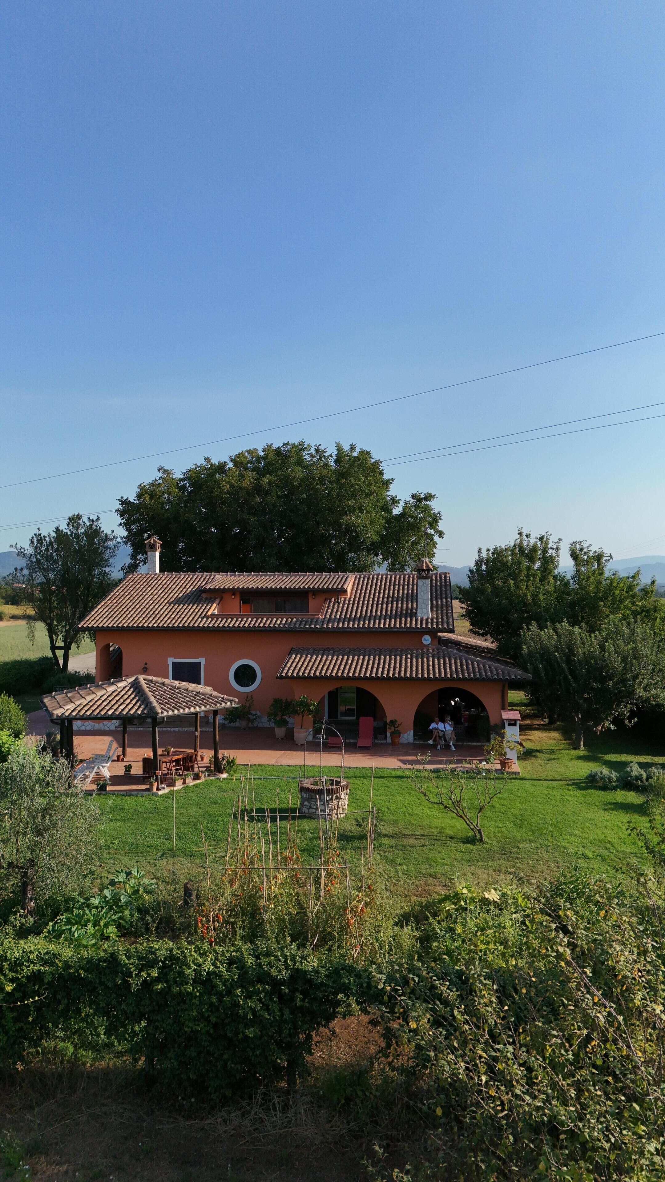 A two-story house with a tiled roof, a patio with outdoor furniture, and a garden in front.