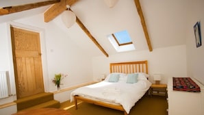 Une chambre avec un lit en bois, une lucarne, une petite table et un banc.