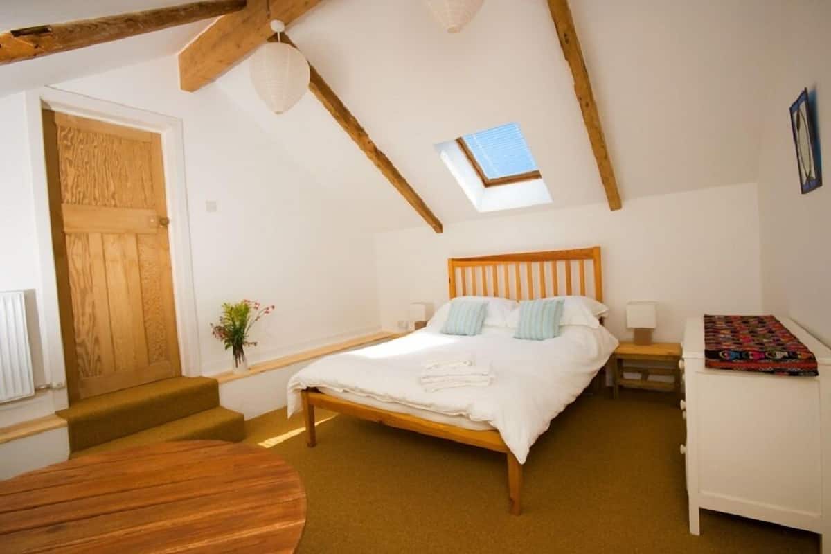 A bedroom with a wooden bed, a skylight, a small table, and a bench.