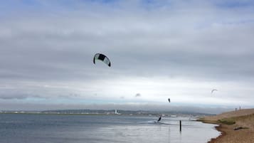 A beach with calm water, a lighthouse in the distance, and a kite surfer in the air.
