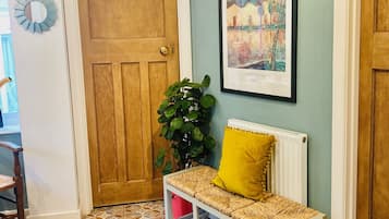 A hallway with a wooden door, a bench with a yellow cushion, a potted plant, and a framed picture on the wall.