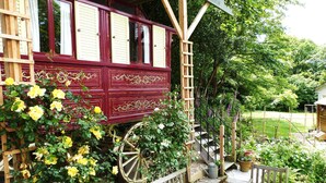 Une structure en bois dotée d’un porche, d’un banc en bois et d’un jardin où poussent des fleurs jaunes.