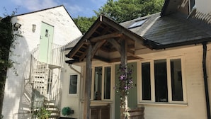 Un bâtiment blanc avec une porte verte, un porche en bois et un escalier menant à un deuxième étage.