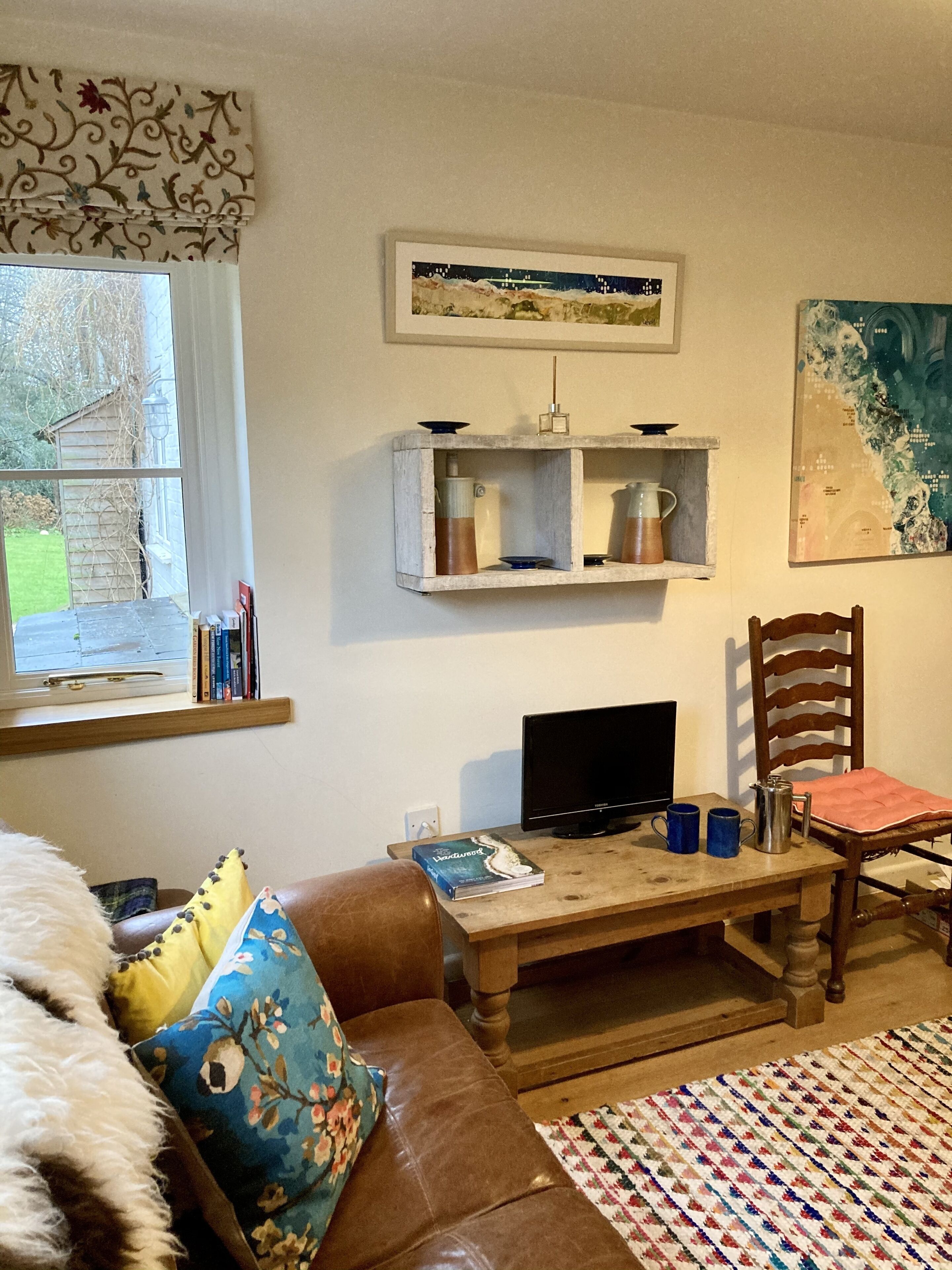 A cozy living room with a brown leather sofa, a wooden coffee table, a television, and a bookshelf with decorative items.