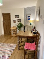 A dining area with a wooden table, chairs, a small potted plant, and framed artwork on the wall.