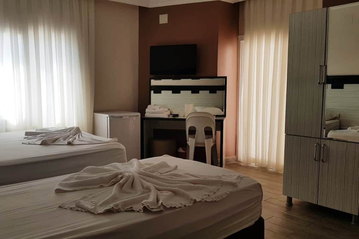 Quarto de hotel com duas camas, uma escrivaninha, televisão e guarda-roupa.