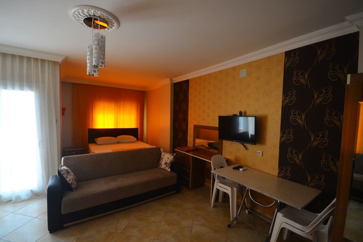 Quarto de hotel com cama, sofá, escrivaninha com cadeira, televisão e janela com cortinas.