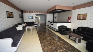 A hotel lobby with a reception desk, black leather sofas, a coffee table, and a tiled floor. - Aslan Apart Otel (Aydincik)