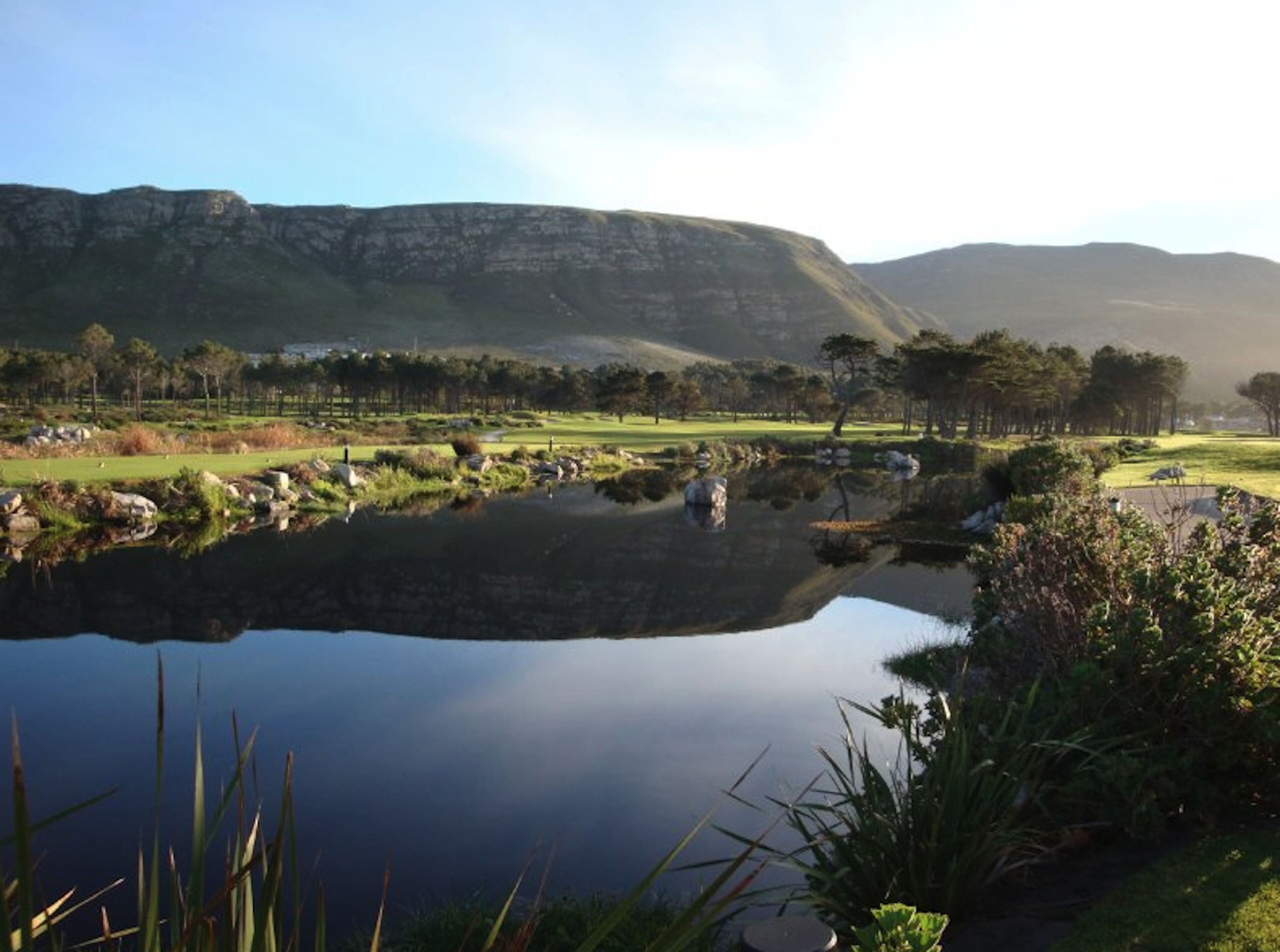 A serene landscape with a calm lake, surrounded by lush greenery and distant mountains.