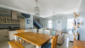 A spacious kitchen with a wooden dining table, white cabinets, and a staircase leading to the upper floor. - The Bicycle Cottage (Hermanus)