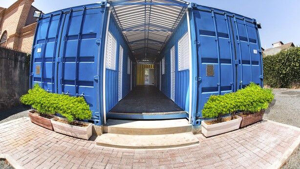 A blue container-like structure with a covered entrance and steps leading up to it. - Residencial Villa Container (Campinas)