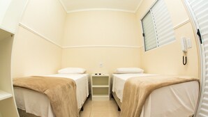 A compact room with two single beds, a small shelf unit, and a telephone. - Residencial Villa Container (Campinas)