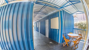A covered outdoor area with blue metal walls, a table with chairs, and a small garden visible through a window. - Residencial Villa Container (Campinas)
